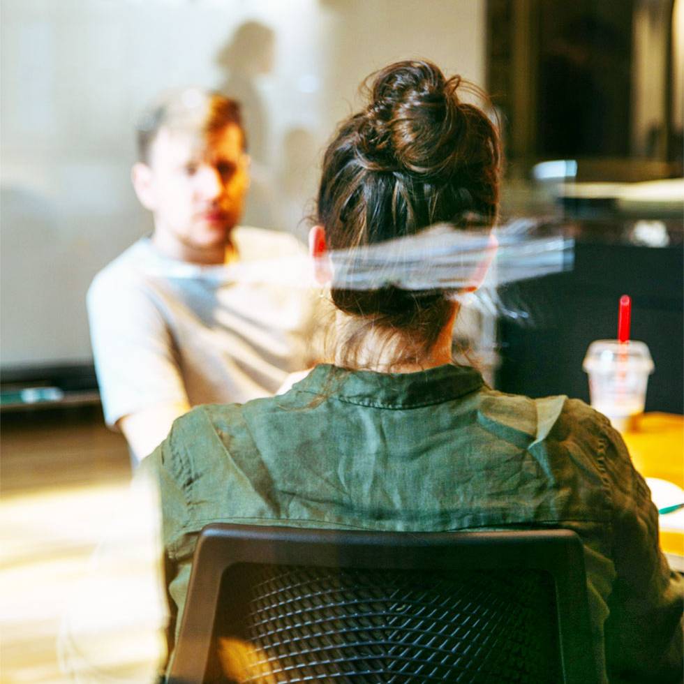 Quelle: Charles Deluvio/unsplash.com Eine Gesprächssituation, bei der sich zwei Personen in einem Café gegenüber sitzen. Es werden ein Mann und eine Frau gezeigt. Die Frau sitzt mit dem Rücken zur Aufnahme, der Mann ist nur verschwommen erkennbar. Beide trinken Kaffee und unterhalten sich.